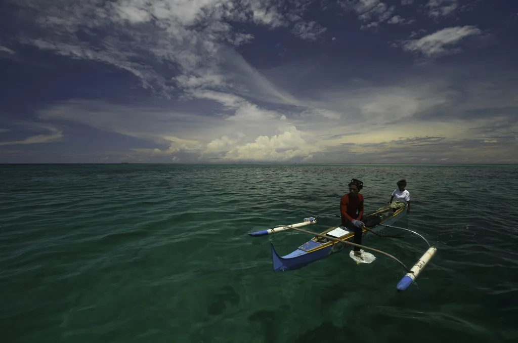 A Bajau Laut fisherman in an outrigger canoe off the coast of Southeast Asia